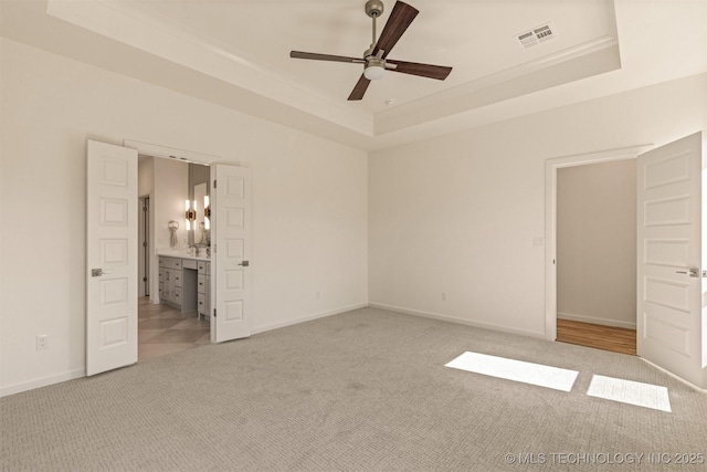 unfurnished bedroom featuring visible vents, baseboards, connected bathroom, light colored carpet, and a tray ceiling