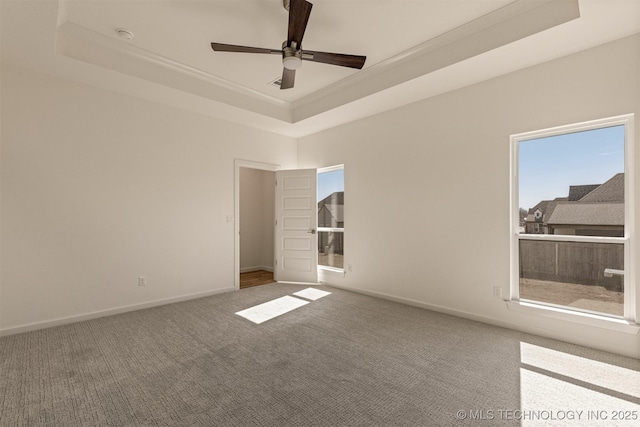 carpeted spare room featuring a raised ceiling, ceiling fan, and baseboards