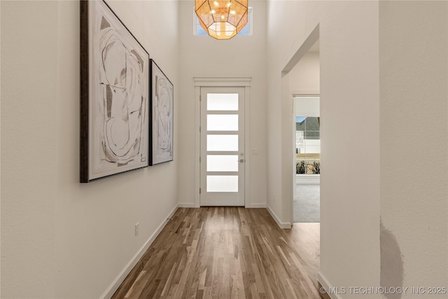 doorway to outside featuring a chandelier, wood finished floors, and baseboards