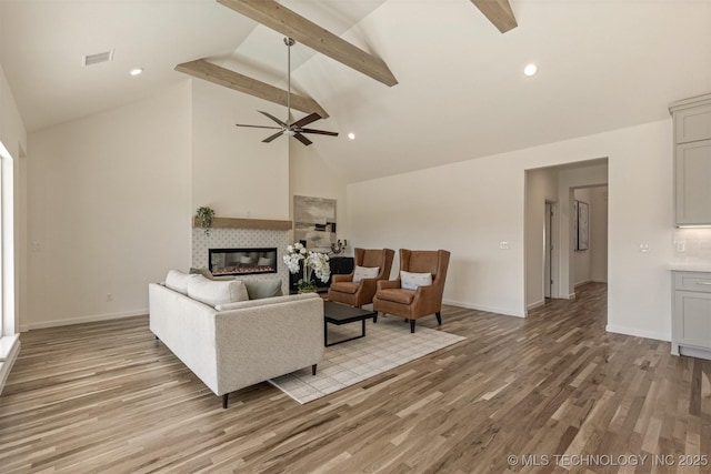 living room featuring light wood-style flooring, visible vents, a tiled fireplace, and beamed ceiling