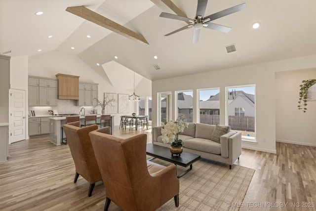 living area featuring ceiling fan, high vaulted ceiling, light wood-style flooring, visible vents, and baseboards