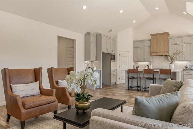 living room featuring high vaulted ceiling, light wood-type flooring, visible vents, and recessed lighting