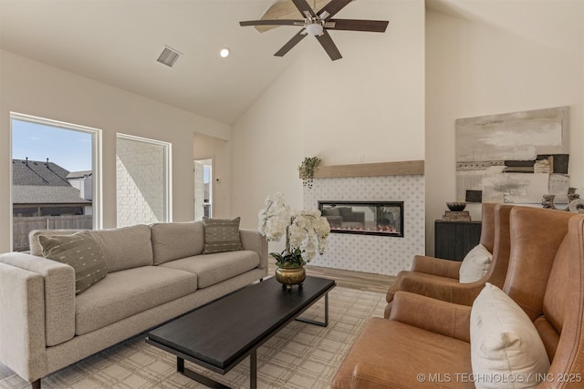 living area featuring a fireplace, visible vents, light wood-style floors, a ceiling fan, and high vaulted ceiling