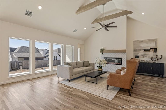 living room with beam ceiling, visible vents, a tiled fireplace, and wood finished floors