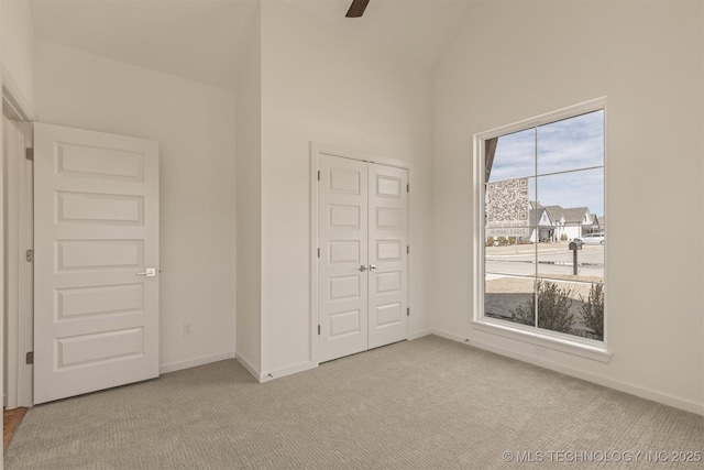 unfurnished bedroom with ceiling fan, lofted ceiling, light carpet, baseboards, and a closet