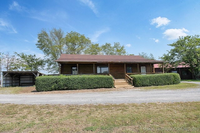 view of front of house with dirt driveway, log exterior, and a detached carport