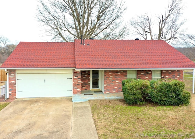 view of front of house featuring a front lawn, concrete driveway, an attached garage, a shingled roof, and brick siding