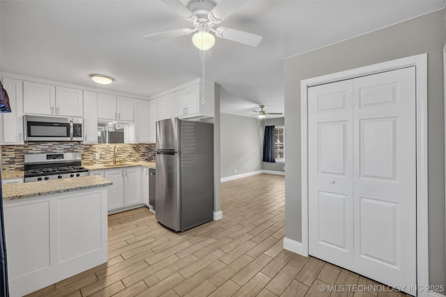 kitchen featuring white cabinets, decorative backsplash, light wood-style flooring, appliances with stainless steel finishes, and light stone counters