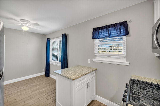 kitchen with light wood finished floors, light stone countertops, a wealth of natural light, and white cabinets