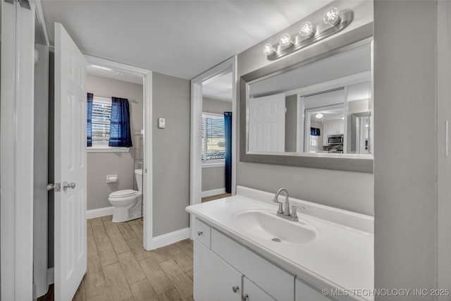 bathroom featuring baseboards, toilet, wood finished floors, vanity, and a healthy amount of sunlight