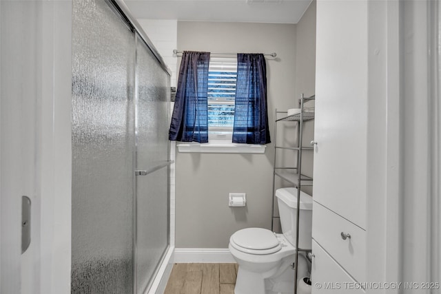 full bathroom featuring baseboards, wood finished floors, toilet, and a shower stall