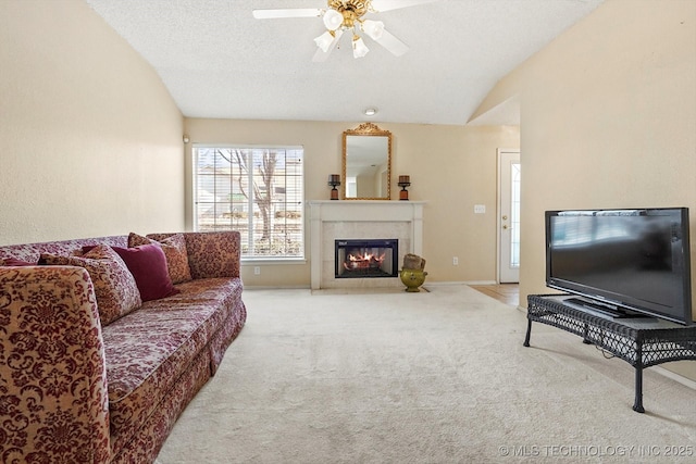 carpeted living room with baseboards, a tiled fireplace, a ceiling fan, lofted ceiling, and a textured ceiling