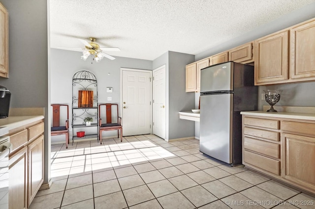 kitchen with light tile patterned floors, light brown cabinetry, light countertops, and freestanding refrigerator