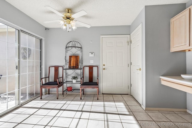 interior space featuring light tile patterned floors, ceiling fan, a textured ceiling, and baseboards