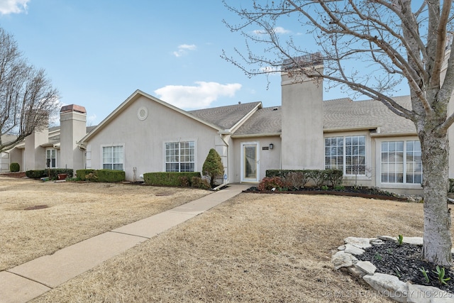 view of front of home with roof with shingles, a chimney, and stucco siding