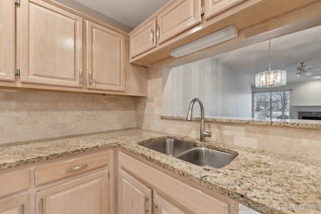 kitchen with a sink, light brown cabinets, light stone countertops, and decorative backsplash