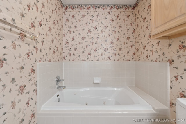 bathroom with toilet, a textured ceiling, a tub with jets, and wallpapered walls