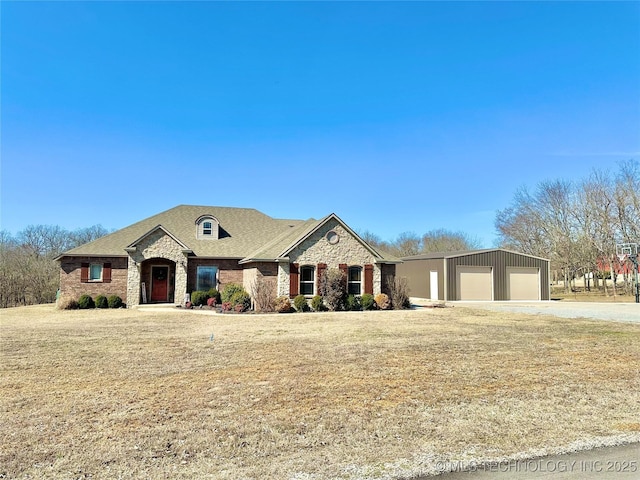 french provincial home featuring an outbuilding, an attached garage, driveway, stone siding, and a front lawn