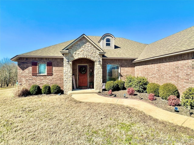 french country style house featuring stone siding, a shingled roof, and brick siding