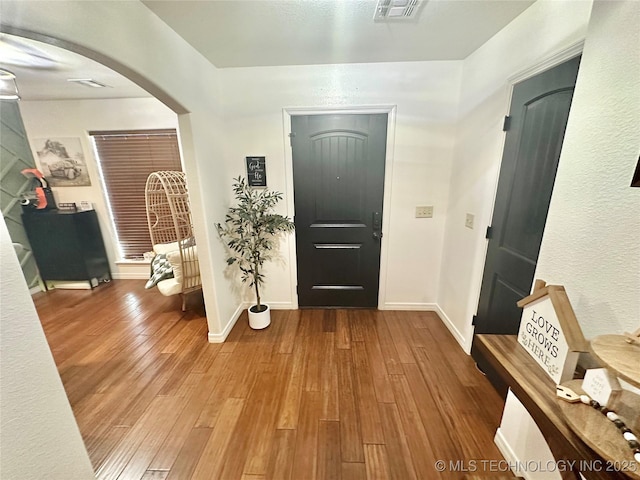 entryway featuring arched walkways, wood-type flooring, visible vents, and baseboards