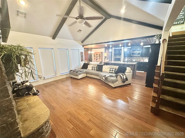 living area with visible vents, ceiling fan, wood finished floors, beamed ceiling, and stairs