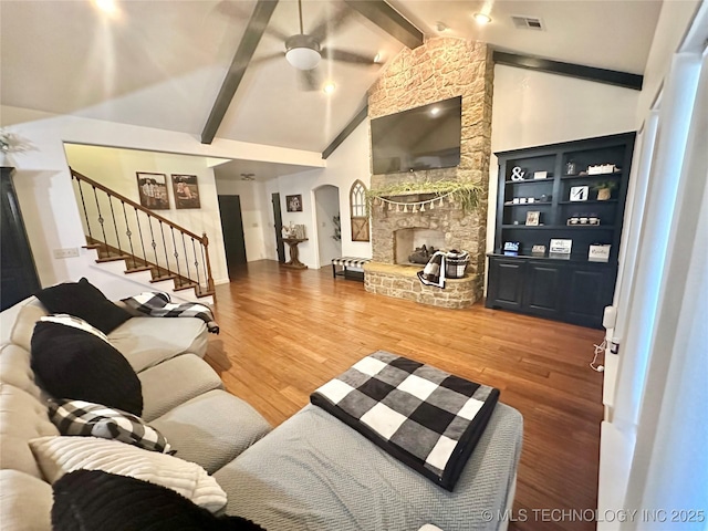 living room featuring a fireplace, wood finished floors, visible vents, stairs, and beamed ceiling