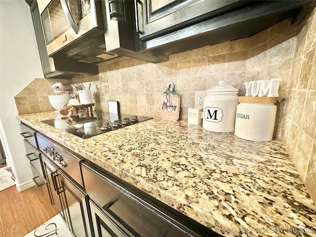 kitchen featuring light wood finished floors, black electric stovetop, stainless steel microwave, decorative backsplash, and light stone countertops