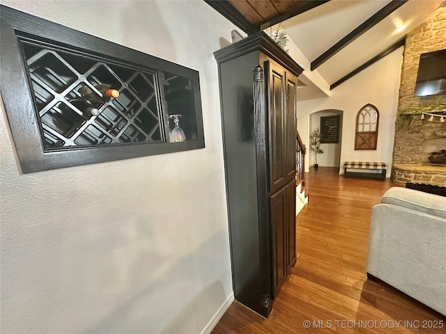 hallway featuring lofted ceiling with beams, arched walkways, wood finished floors, and baseboards