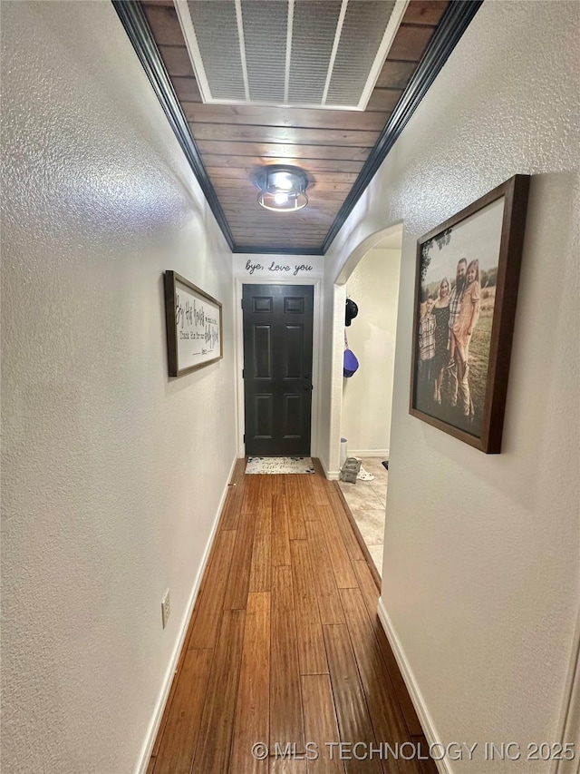 hallway featuring arched walkways, crown molding, visible vents, wood finished floors, and baseboards