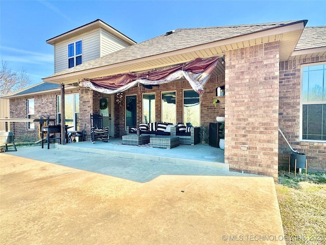 back of property featuring a shingled roof, a patio area, brick siding, and an outdoor hangout area