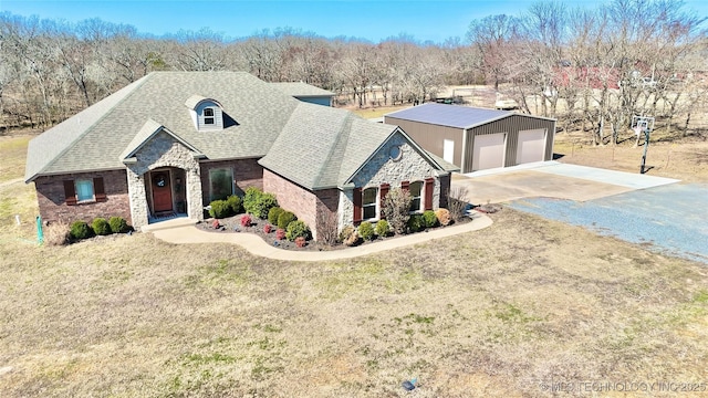 french country style house with an outbuilding, roof with shingles, a front yard, a garage, and stone siding