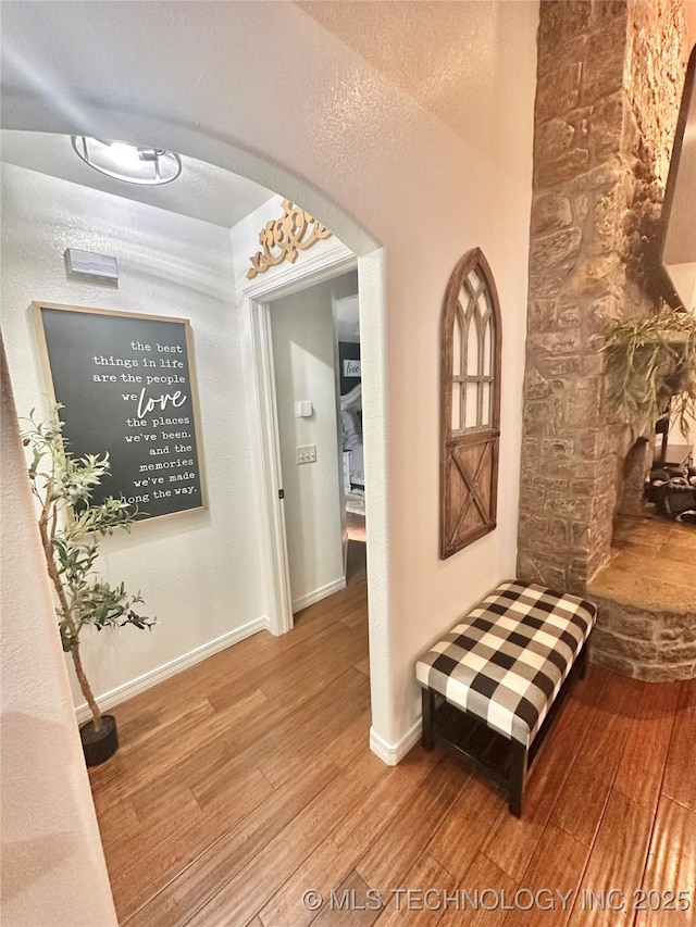 hall featuring arched walkways, wood finished floors, and baseboards