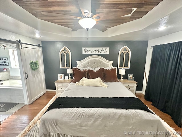 bedroom featuring a barn door, baseboards, a raised ceiling, ceiling fan, and wood finished floors