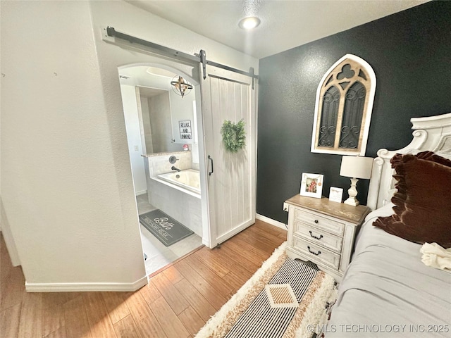 bedroom with arched walkways, wood finished floors, baseboards, and a barn door