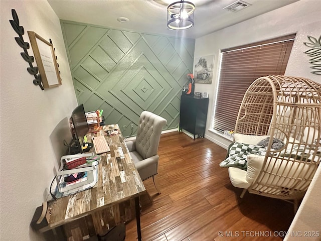 home office featuring an accent wall, wood finished floors, visible vents, and baseboards