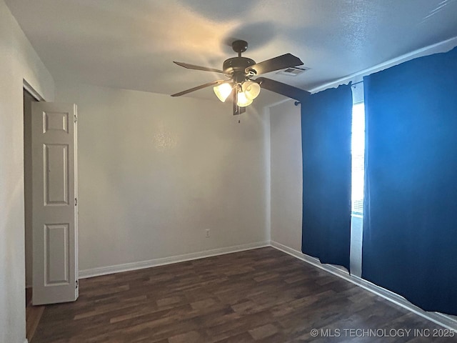 spare room featuring ceiling fan, dark wood-style flooring, visible vents, and baseboards