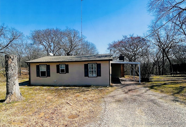 view of front of property with a carport, dirt driveway, and a chimney