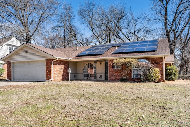 ranch-style home featuring brick siding, an attached garage, covered porch, roof mounted solar panels, and a front yard