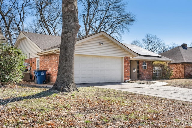 view of front of house with brick siding, solar panels, a shingled roof, an attached garage, and driveway