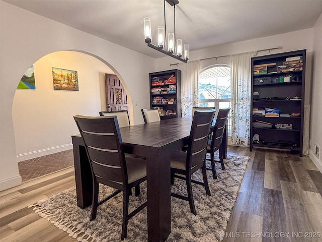 dining room with an inviting chandelier, baseboards, arched walkways, and wood finished floors