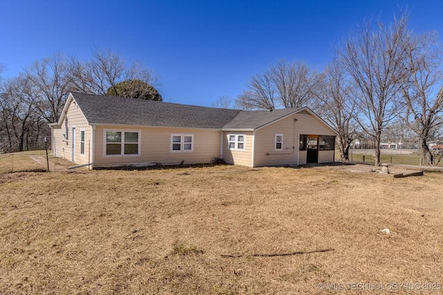 back of property with a shingled roof and a lawn