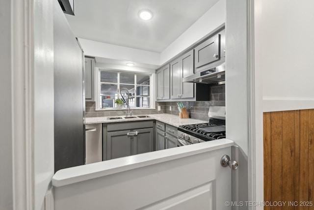 kitchen featuring light countertops, backsplash, gray cabinetry, appliances with stainless steel finishes, and under cabinet range hood