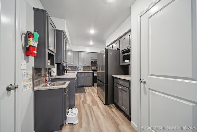 kitchen with gray cabinetry, a sink, light wood-style floors, appliances with stainless steel finishes, and tasteful backsplash