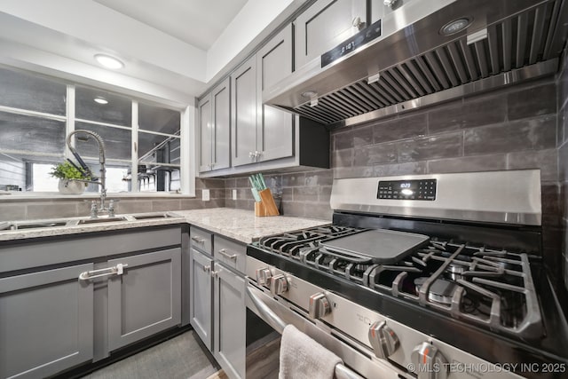 kitchen featuring stainless steel gas stove, tasteful backsplash, extractor fan, gray cabinetry, and a sink