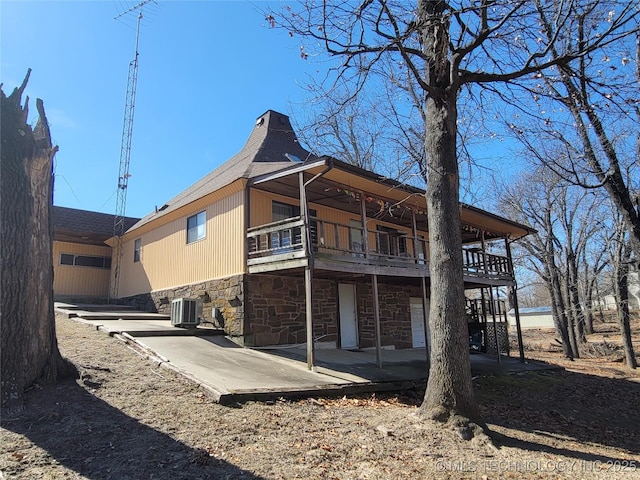 rear view of property with a patio area, stone siding, central AC, and a wooden deck