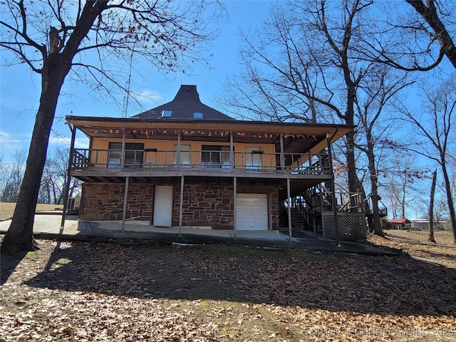 rear view of property with a garage, stone siding, stairs, a deck, and a patio area