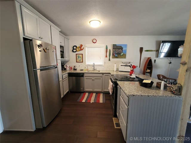 kitchen featuring appliances with stainless steel finishes, light stone counters, dark wood-type flooring, a peninsula, and a sink