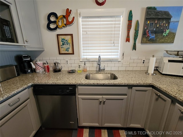 kitchen with a sink, backsplash, stainless steel dishwasher, and light stone countertops