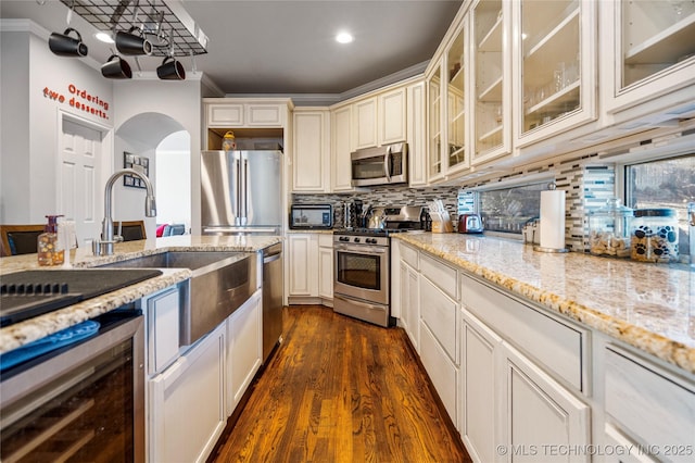 kitchen featuring tasteful backsplash, beverage cooler, stainless steel appliances, cream cabinetry, and a sink