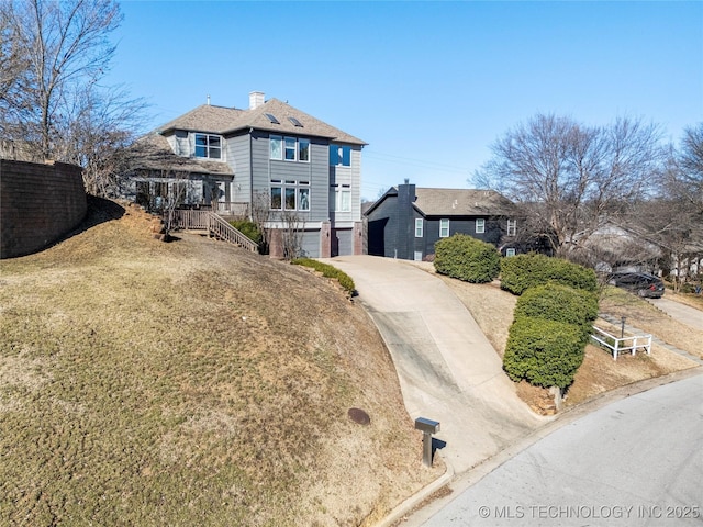 view of front facade with driveway, a chimney, an attached garage, and fence